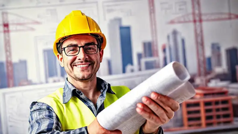 Ingeniero civil sonríe con planos y casco